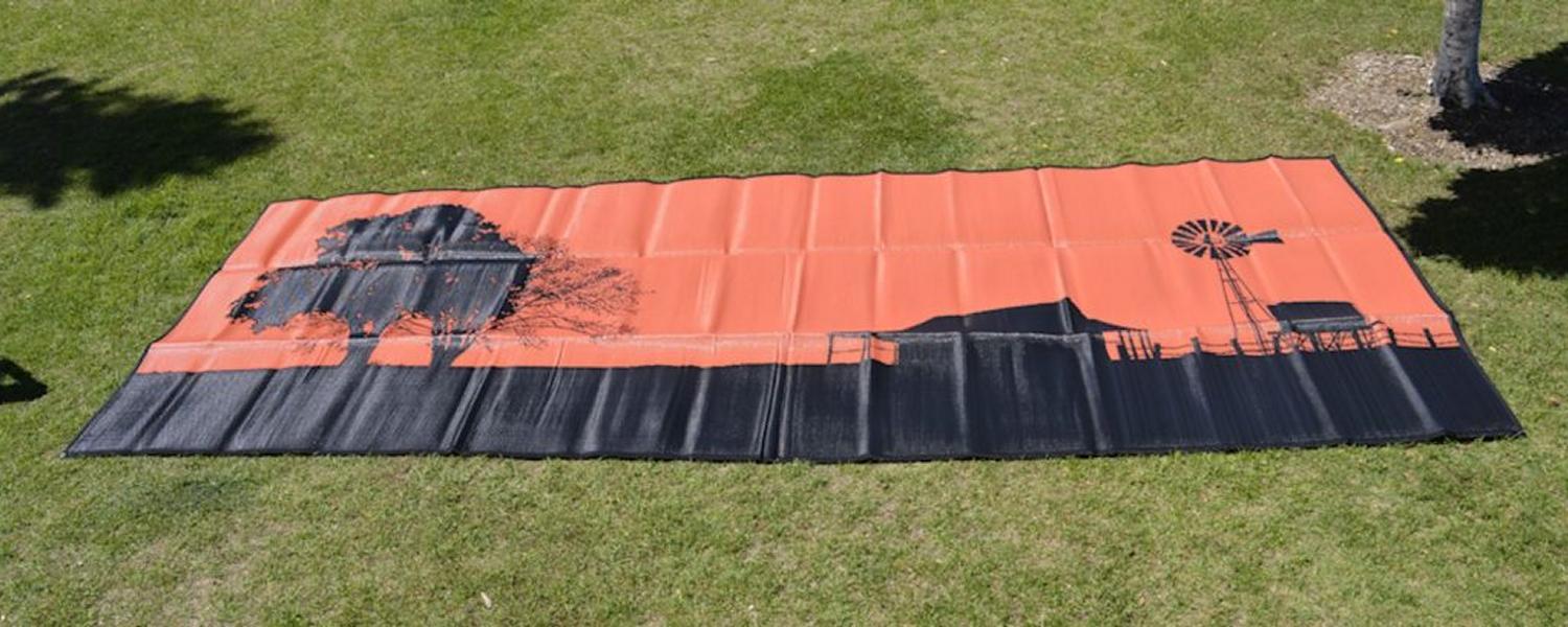 Jawa Off Road Camper Trailer camping mat laid out. "Homestead" is an orange and black mat depicting a simple shack, tree and windmill in the Australian country. Available in various sizes in Sunshine Coast Queensland.