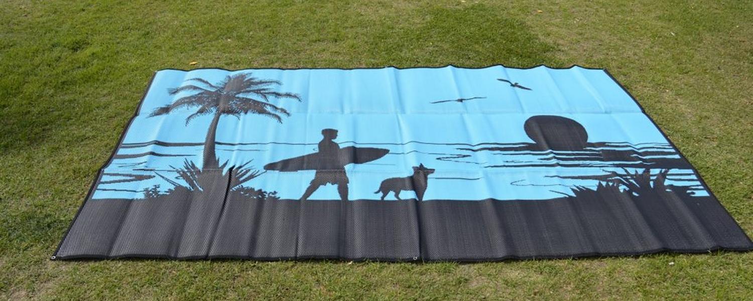 Jawa Off Road Camper Trailers Sunshine Coast Queensland camping mat for caravan. "Morning Surf" is a black and blue mat picturing a dog and a man with his surfboard on an Australian beach with palm trees.