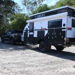 Jawa Solera 15 Solid pop top off road camper, easy setup caravan for couples. Pictured parked at dirt campsite with trees in background attached to four wheel drive with roof popped up.