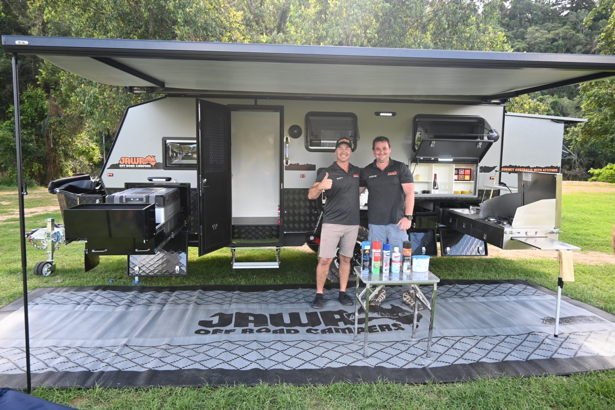 Jawa Infinity 15 hybrid off road camper, large camper for family of four, pictured fully set up at grassy campsite with two men smiling posing arm in arm for the camera. Awning, fridge slide, pantry and external cooktop are all set up ready for use.