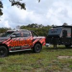 Jawa Infinity Escape hybrid off road camper trailer, large and spacious camper for couples, pictured in grassy area towed by four wheel drive ute covered in Jawa branding.