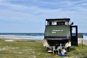 Jawa Off Road Camper Trailer, the Stealth 12, parked on some grass from an adventure by the ocean. Fully set up with roof popped up and alfresco kitchen. Get this tough caravan in Sunshine Coast Queensland.