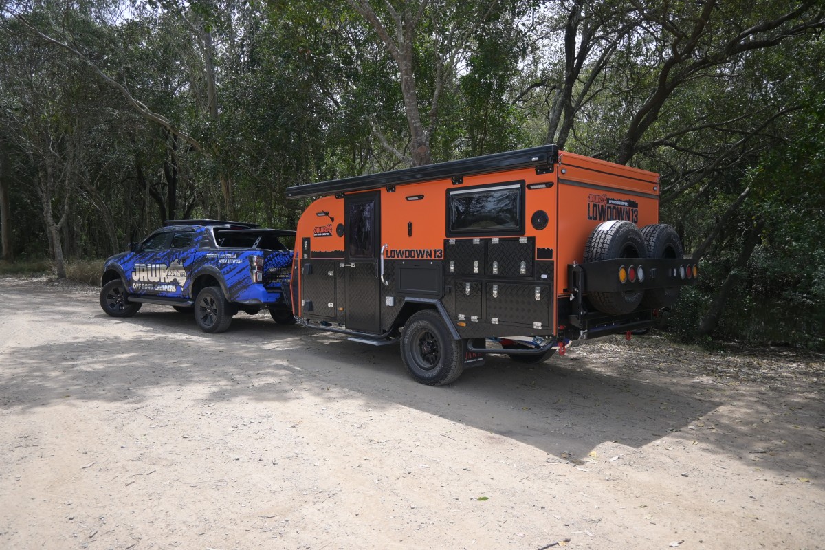 Jawa Lowdown 13 Cupboard low hybrid poptop off road camper with lots of storage perfect for adventuring couples and storing in standard garage, pictured at bushland campsite towed by blue four wheel drive ute covered in Jawa branding, far back view.