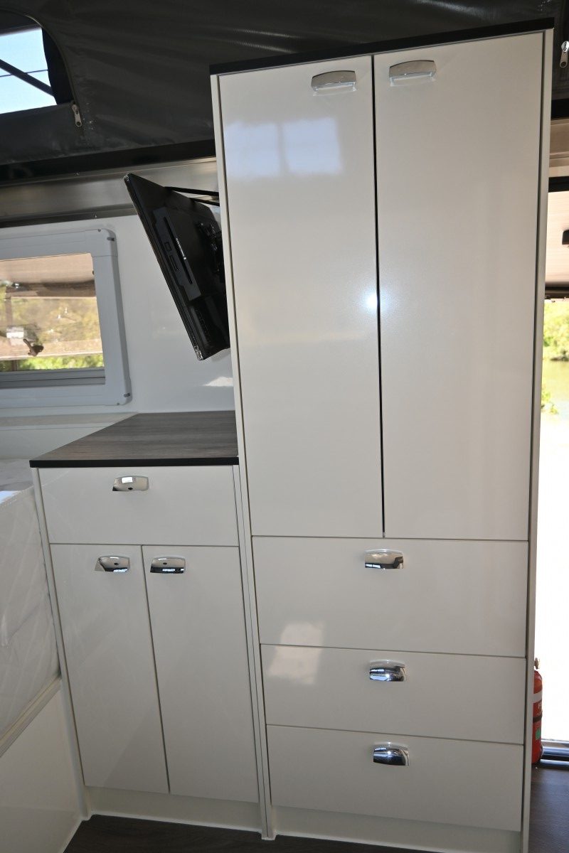 Jawa Infinity 13 hybrid off road camper for three person family, pictured inside with full wardrobe for good storage and TV pack mounted to it facing the bed.