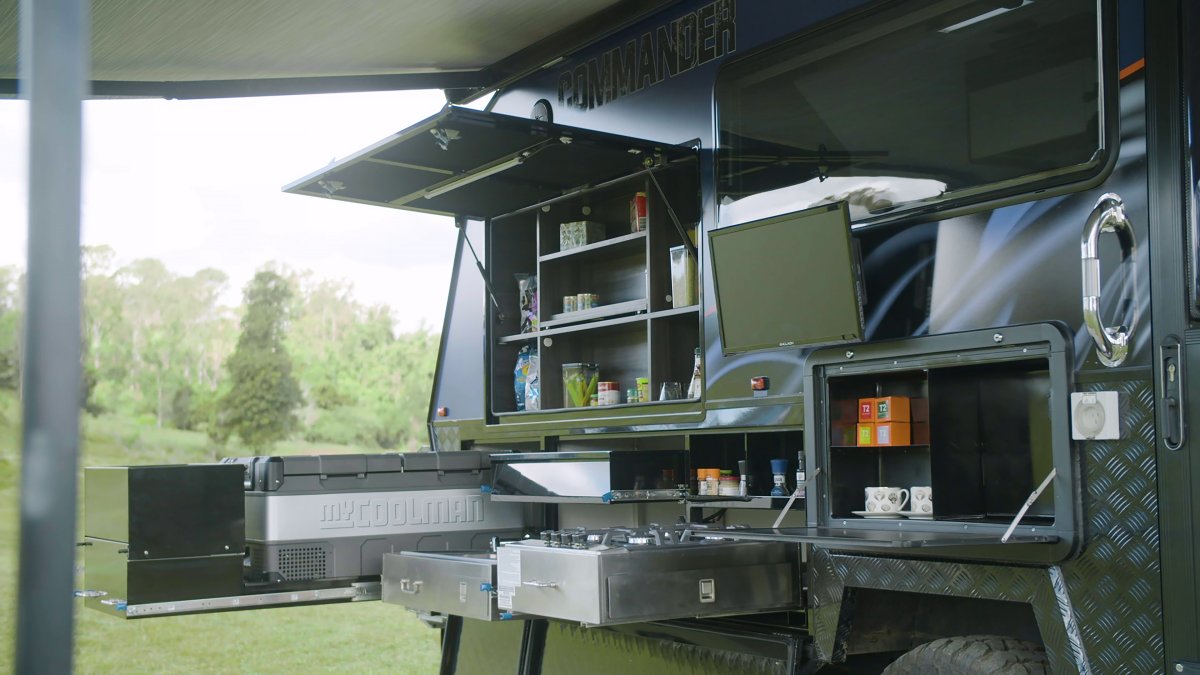 Jawa Commander hardtop off road camper with exterior fridge slide and kitchen. Pictured with storage doors open with some groceries and small television for entertainment, close up view.