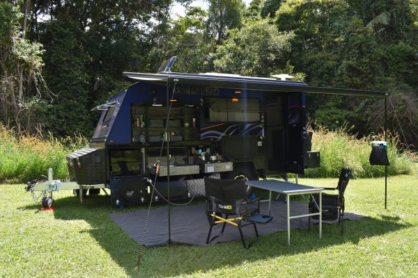 Jawa Camper Trailers Commander hard top caravan, side view with camping set up. Camping mat, awning and camping chairs and table are set up. Caravan and other features available at Sunshine Coast Queensland.
