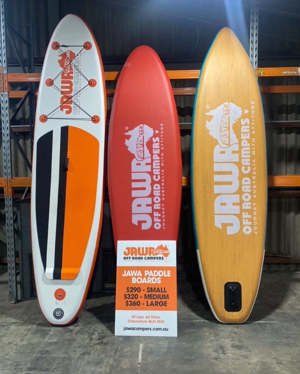 Three paddle boards with Jawa Off Road Camper Trailers logos on them. Ordered from left to right, large, small and medium. Large one is $360 orange, white and black. Medium is $320 with a wooden look. Small is $290 and red. For sale at Sunshine Coast Queensland.