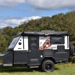Jawa Stealth 10 hybrid compact off road camper trailer, small size camper for couples, parked on grass with hilly and bush landscape behind.